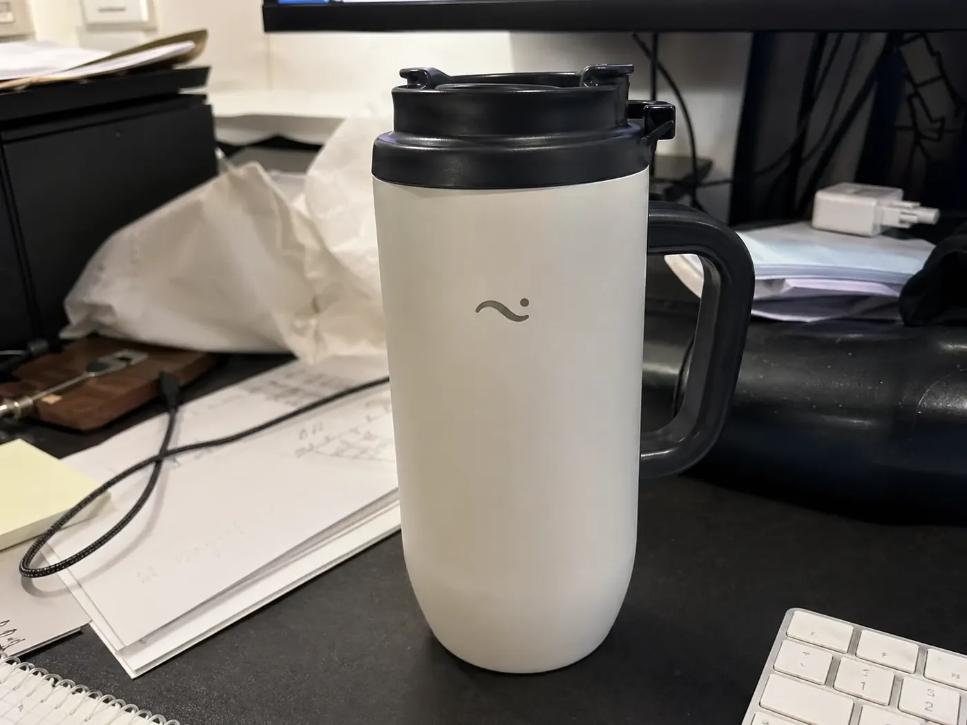 Input product photo of a reusable travel mug on a cluttered desk before ChatGPT editing.